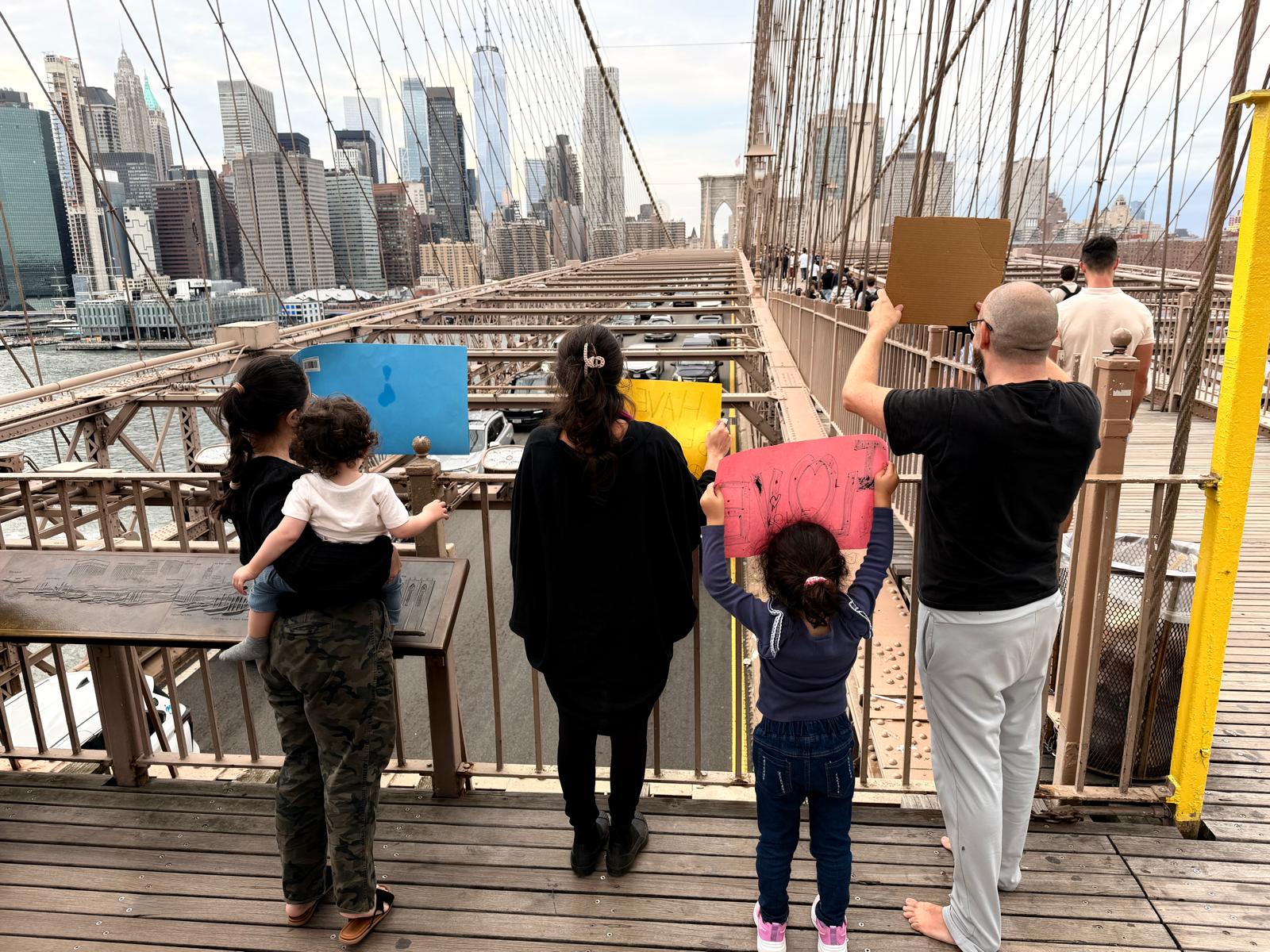 Our group holding kindness signs beside the Brooklyn Bridge railing, with the Manhattan skyline ahead